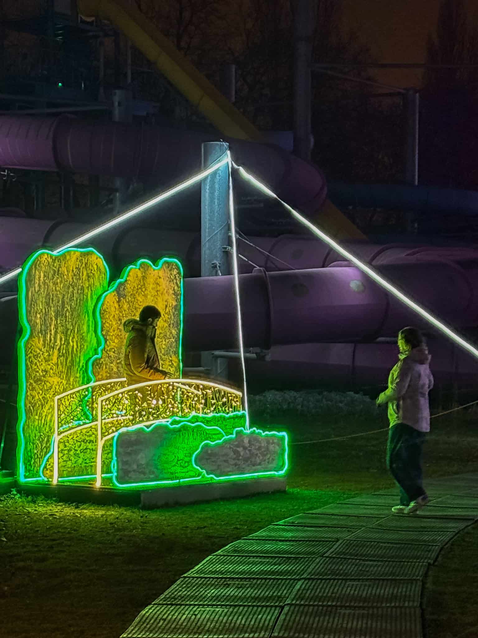 A glowing green wooden bridge safely spanning a calm reflective water channel