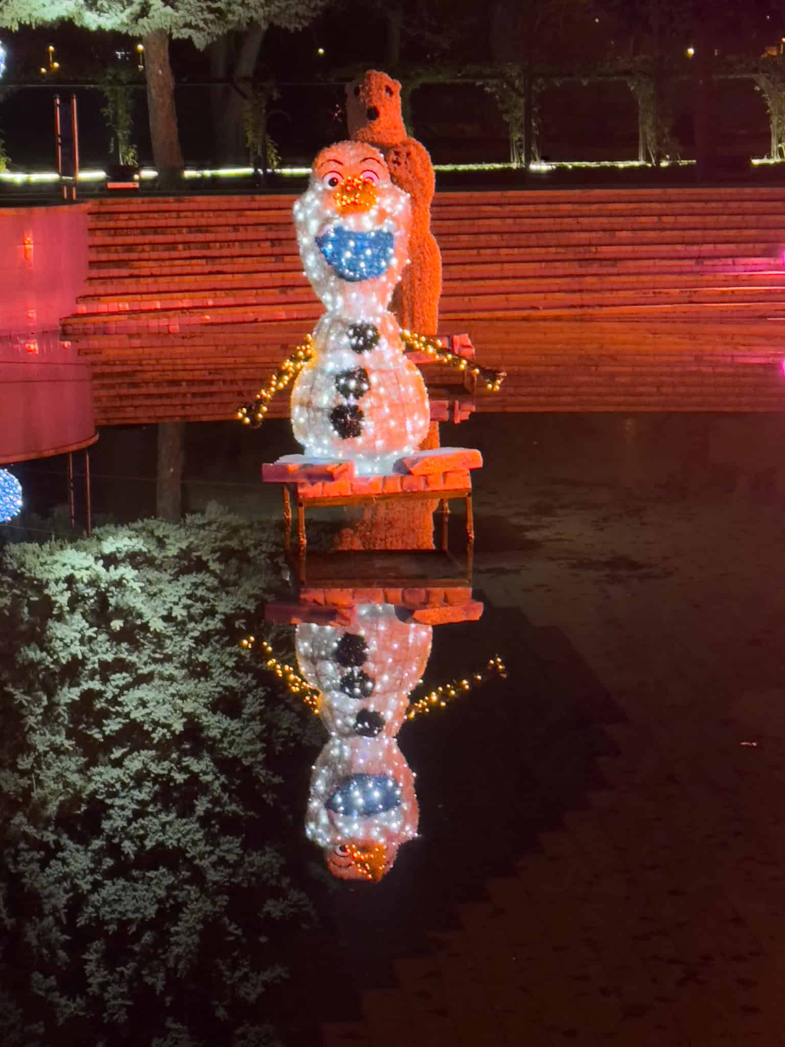 A whimsical glowing snowman built entirely from bent wire frames and warm LED lights