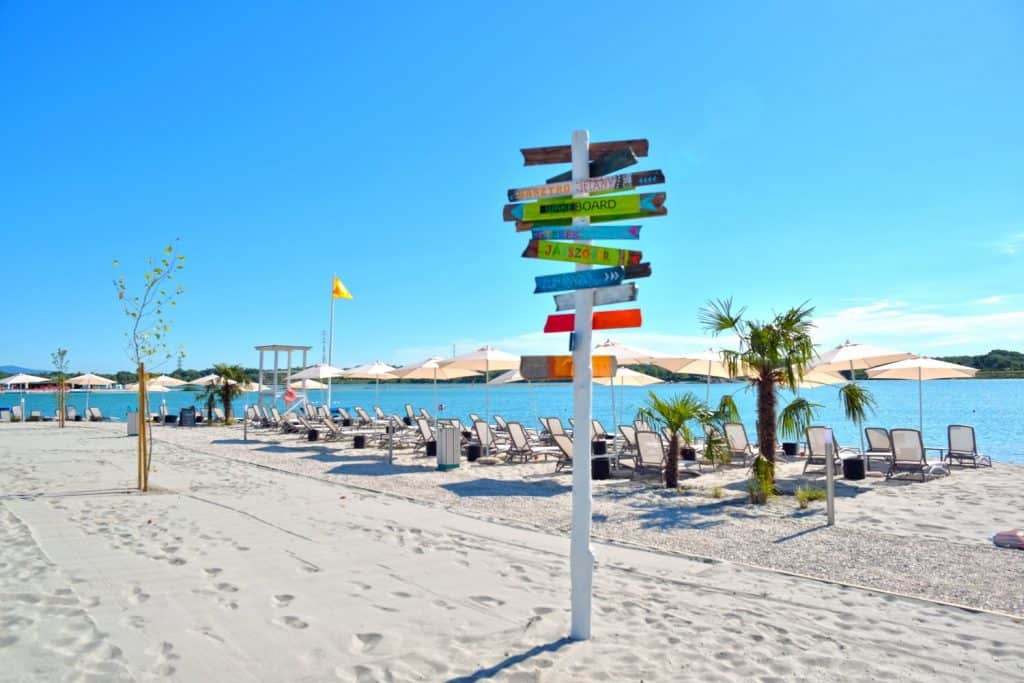 A colourful wooden signpost on the white sand of Lupa Beach
