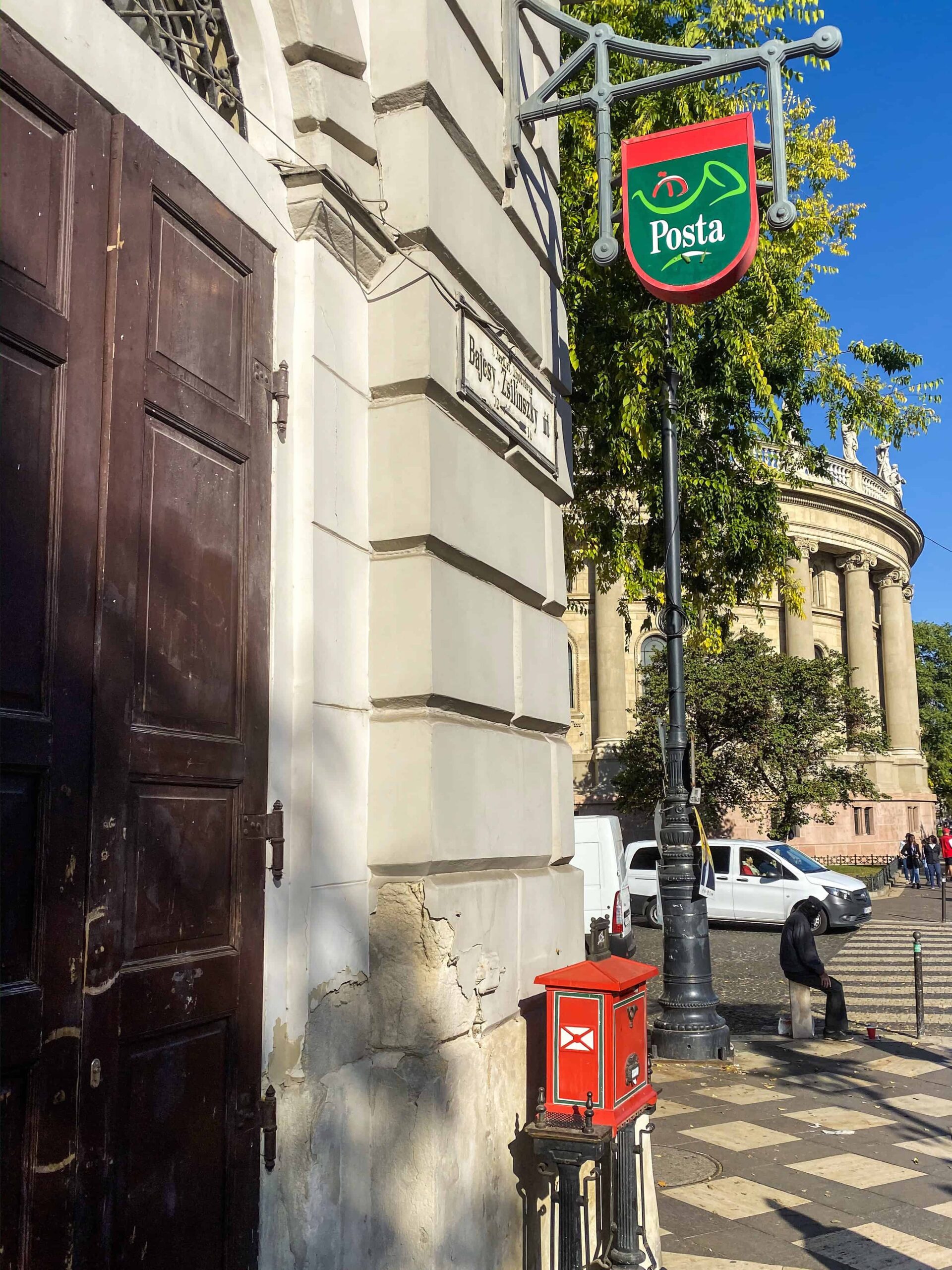 A hand dropping a postcard into a red Hungarian letterbox
