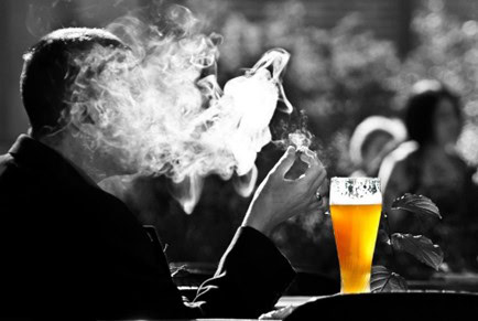 A man smoking a cigarette and drinking a beer outdoors