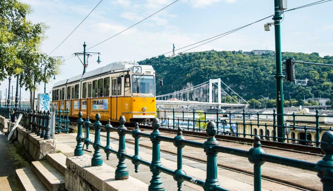 A classic long yellow public tram confidently speeding securely across the wide bridge