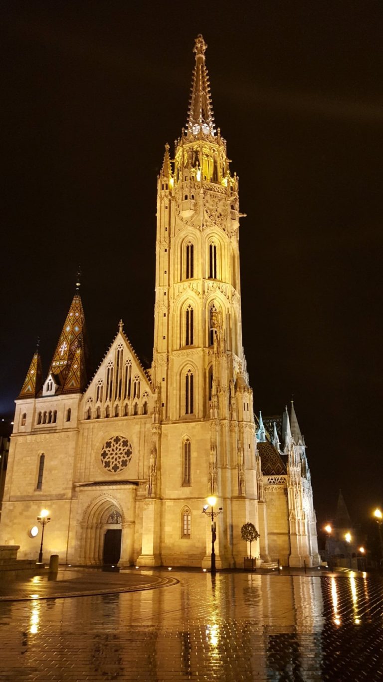 The tall intricate stone gothic spire of Matthias Church piercing through heavy rain clouds