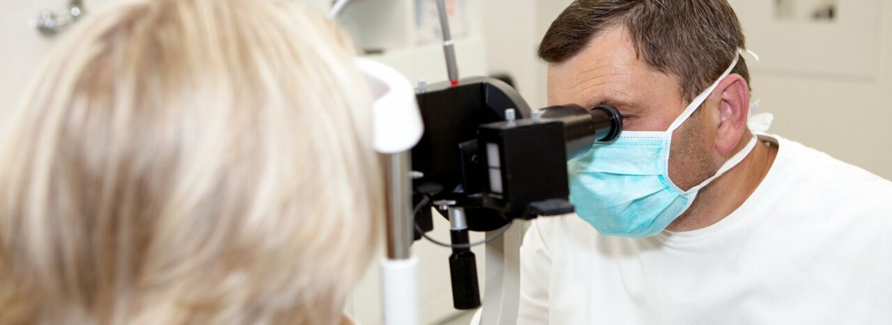 A doctor in a mask conducts an eye examination with a patient