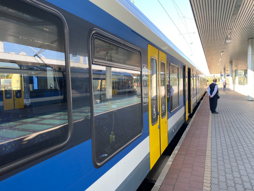 A modern blue and yellow Hungarian MAV passenger train stopped at a platform