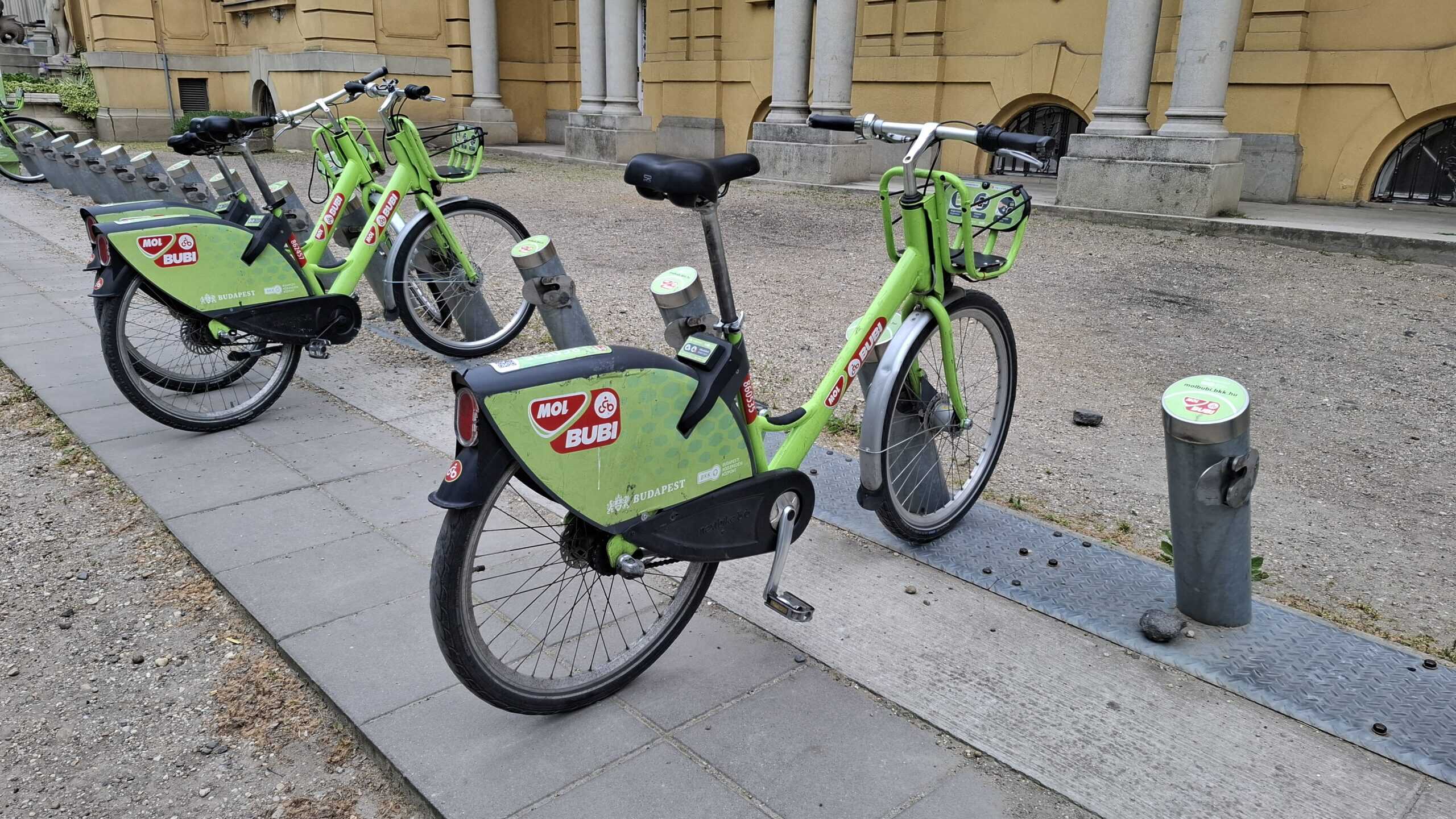Green MOL Bubi shared bicycles parked at a docking station in front of the Széchenyi Thermal Bath in Budapest.