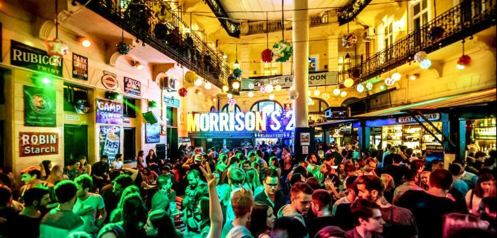 A dense energetic crowd of young people actively dancing under bright flashing neon lights inside Morrison's 2