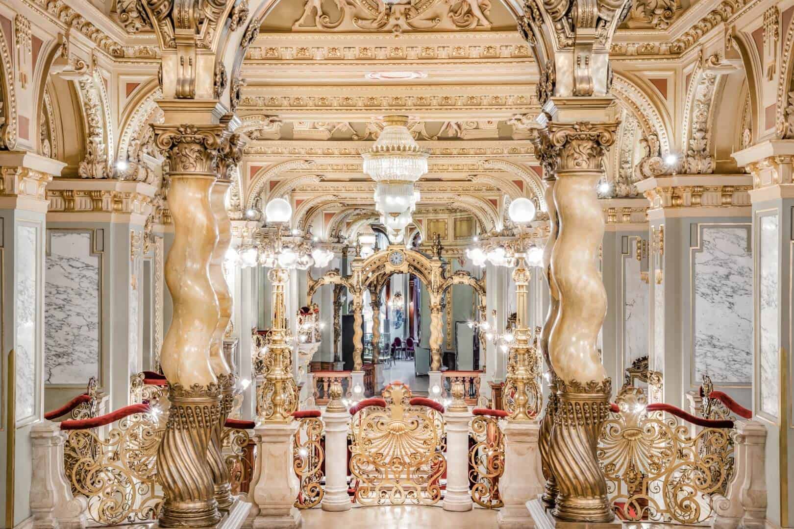 The sweeping ornate twisted marble columns and intricate golden stairway railings of the majestic New York Cafe