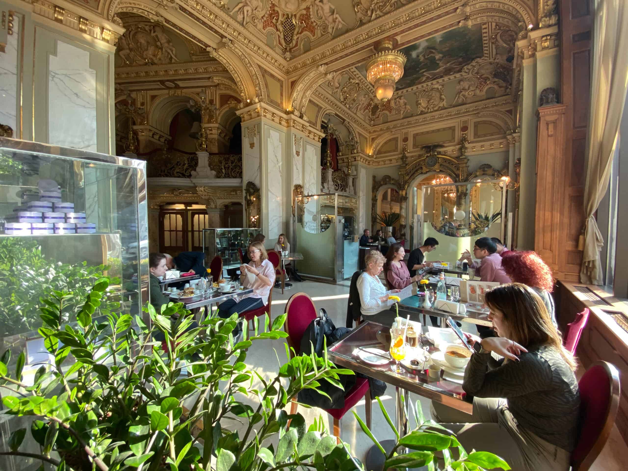 Patrons comfortably sitting at small sunlit tables actively enjoying luxury coffee and pastries