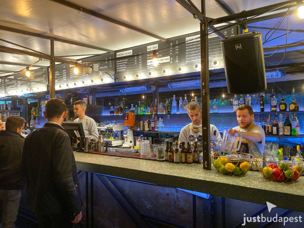 Bartenders actively mixing fresh drinks at a busy outdoor rooftop bar counter at night