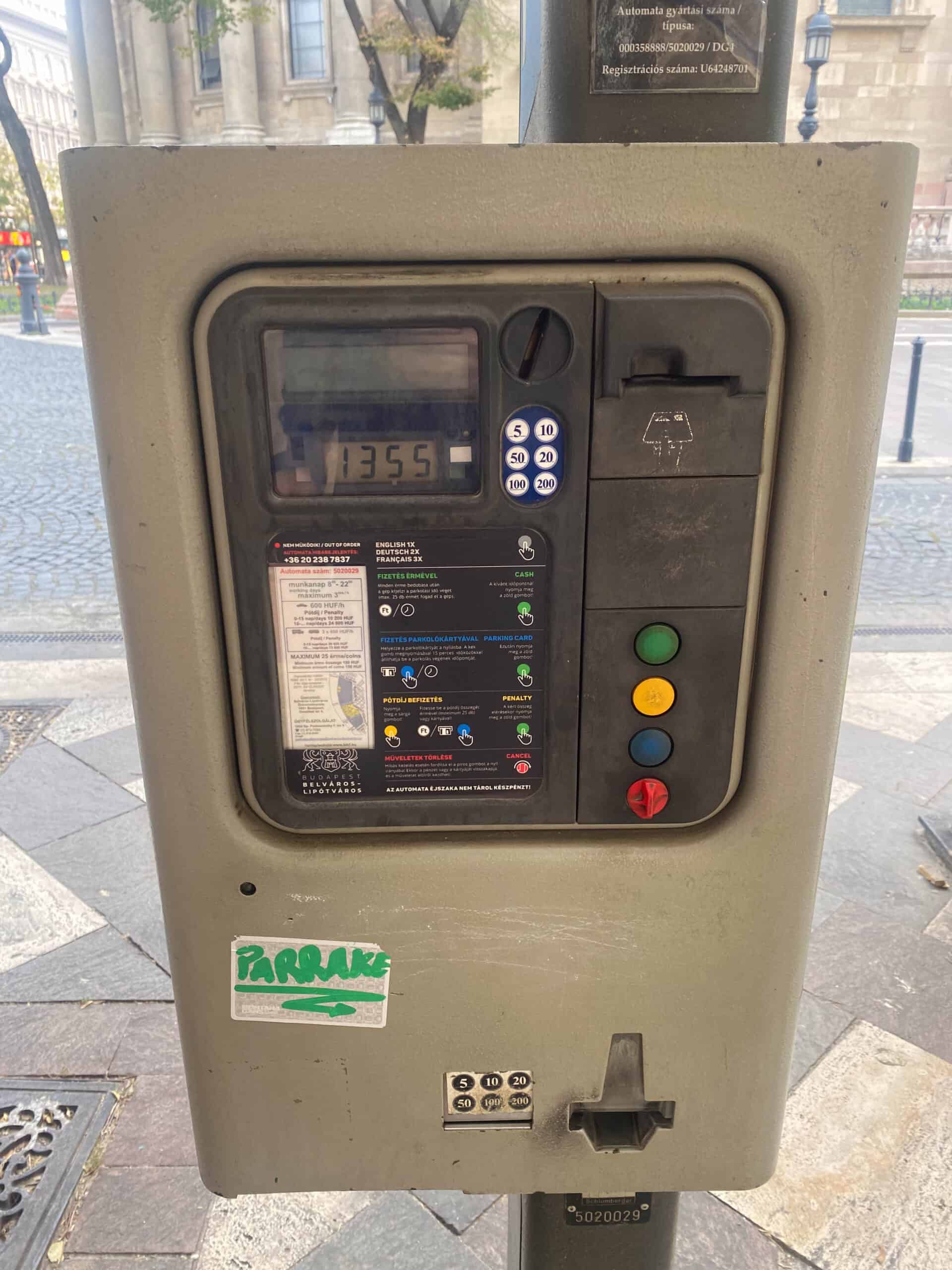 A close up of a worn older gray parking meter machine showing the coin slot and digital display