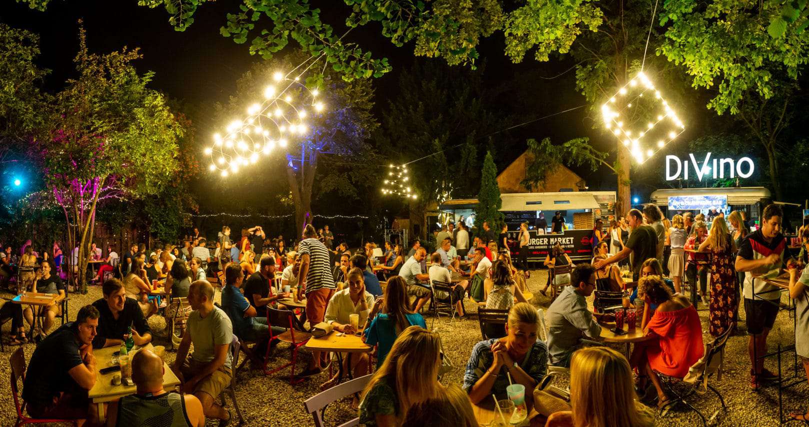 A bustling outdoor gravel garden with food trucks and string lights at night