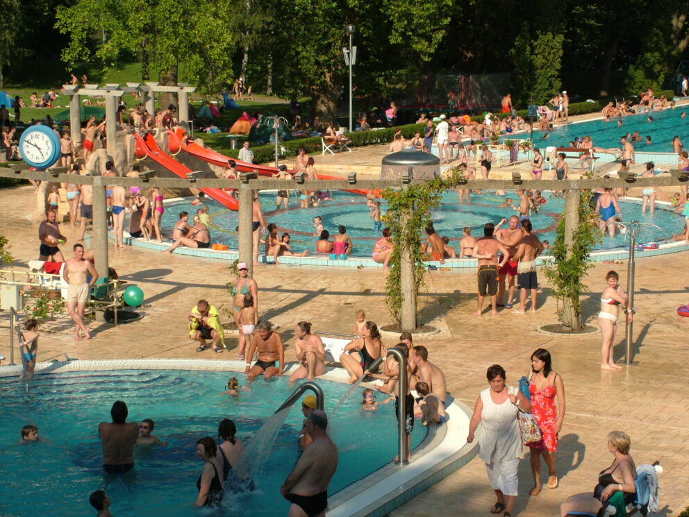 A crowded outdoor summer bath complex featuring a blue pool and red slide