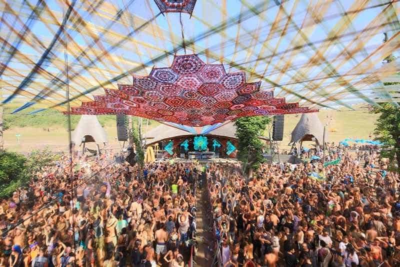 An elevated view of the main stage canopy casting shade over a huge sprawling crowd of dancers