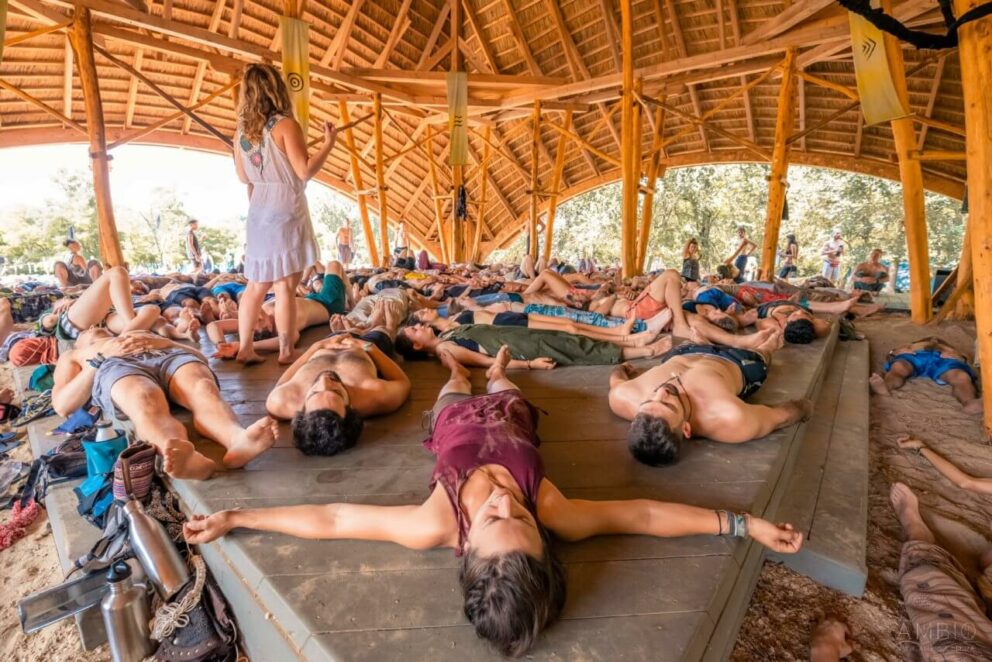 Dozens of people lying on their backs relaxing inside a large open-air wooden pavilion during a workshop