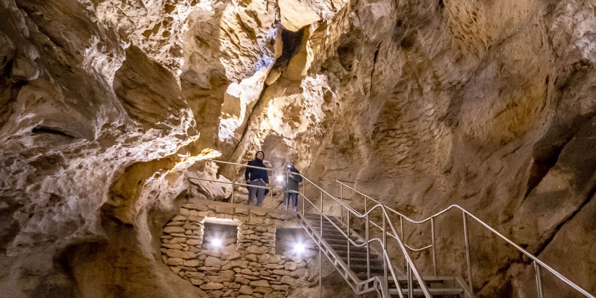 Two tourists exploring the illuminated rock walls of Pal-volgyi Cave from a stone viewing platform