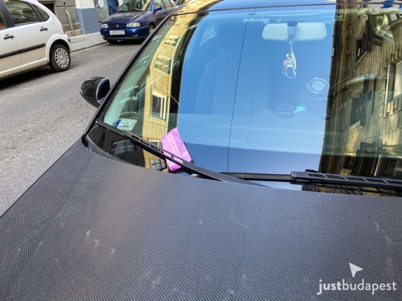 A pink penalty parking ticket tucked under the windshield wiper blade of a parked car