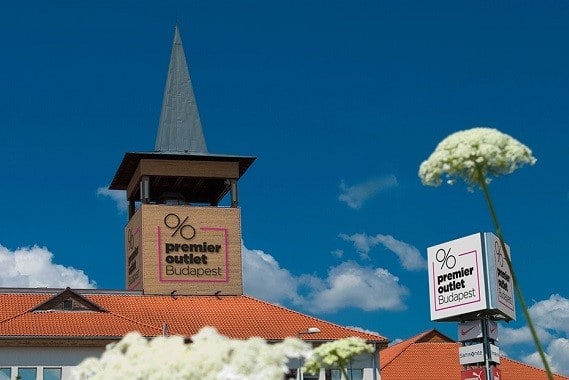 The central square of Premier Outlet featuring the iconic brick tower, flowers, and the visitor map