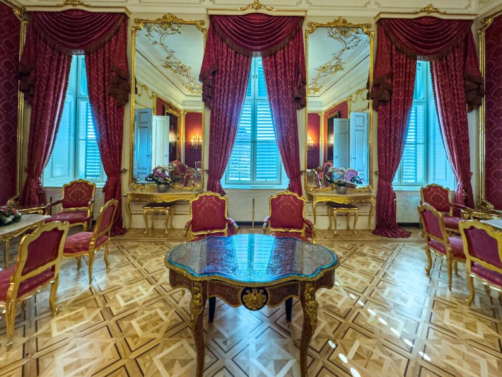 Wide view of the grand Red Salon with a crystal chandelier and portraits