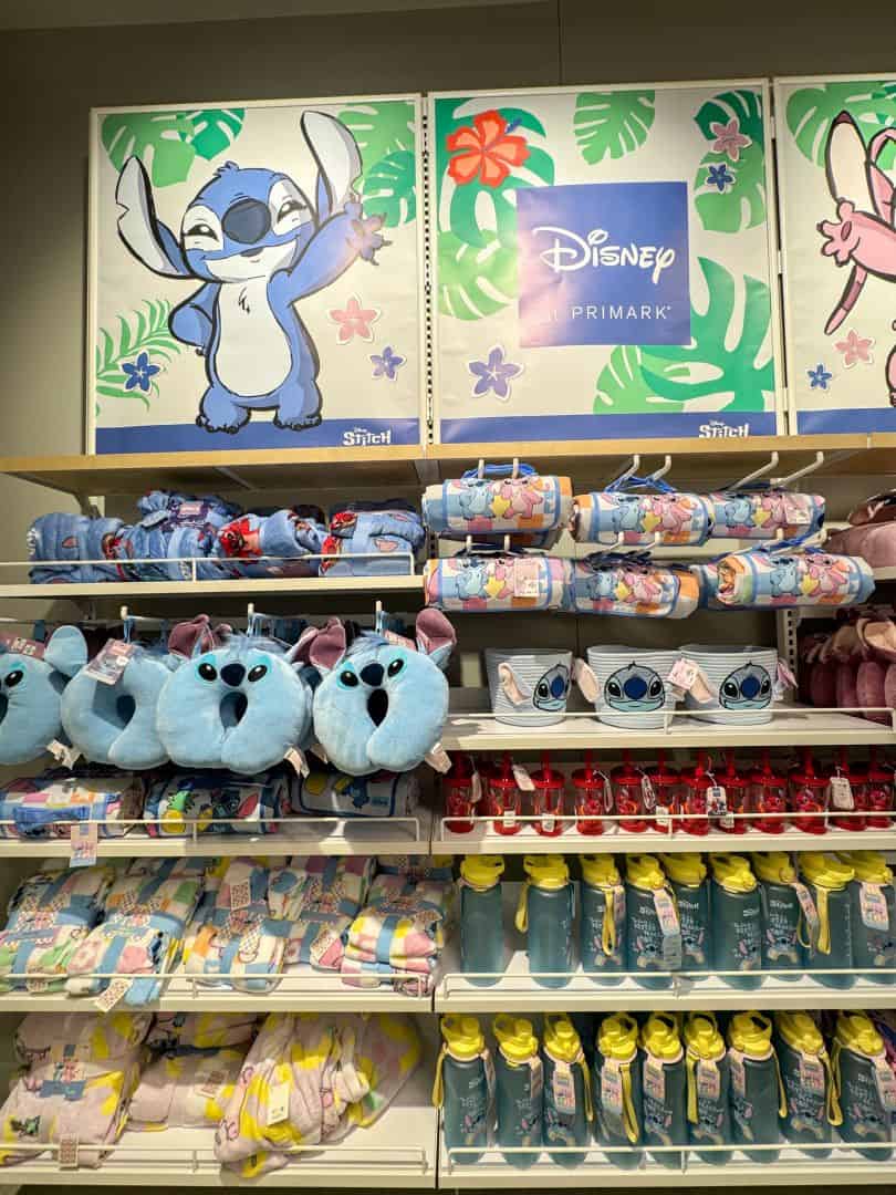 A shelf full of Lilo and Stitch Disney merchandise including neck pillows and blankets