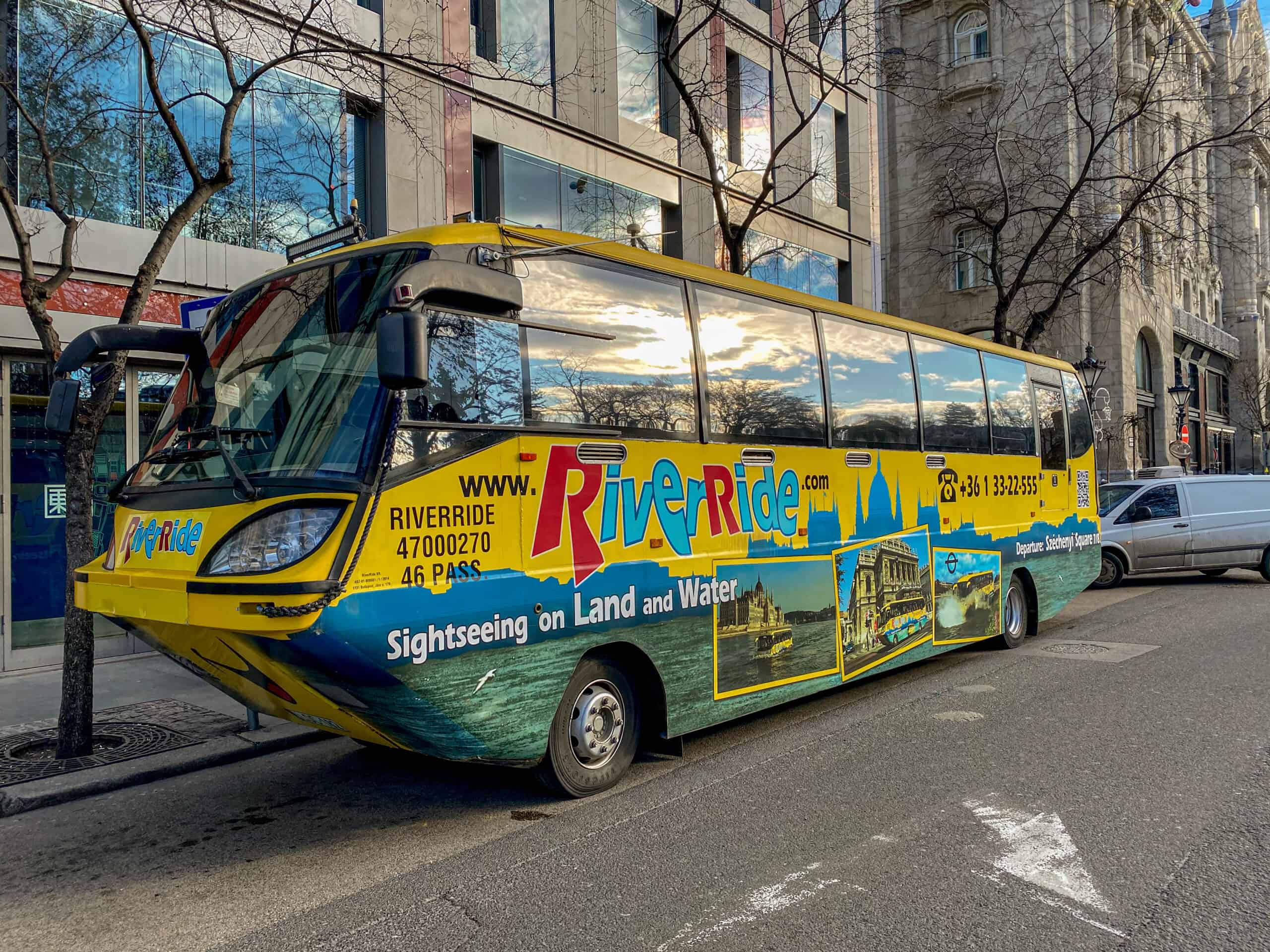 The yellow and blue RiverRide amphibious sightseeing bus parked on a Budapest street on a sunny day.