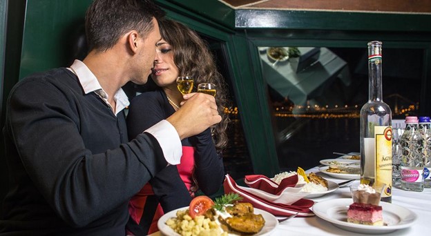 A couple enjoying a romantic dinner and drinks on a night cruise