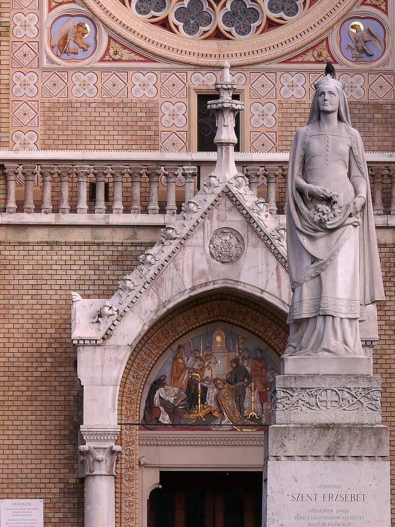 A stone statue of Saint Elizabeth holding roses in front of a church in Budapest