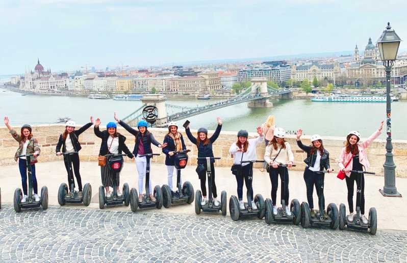 A Segway tour group waving with a panoramic view of the Danube