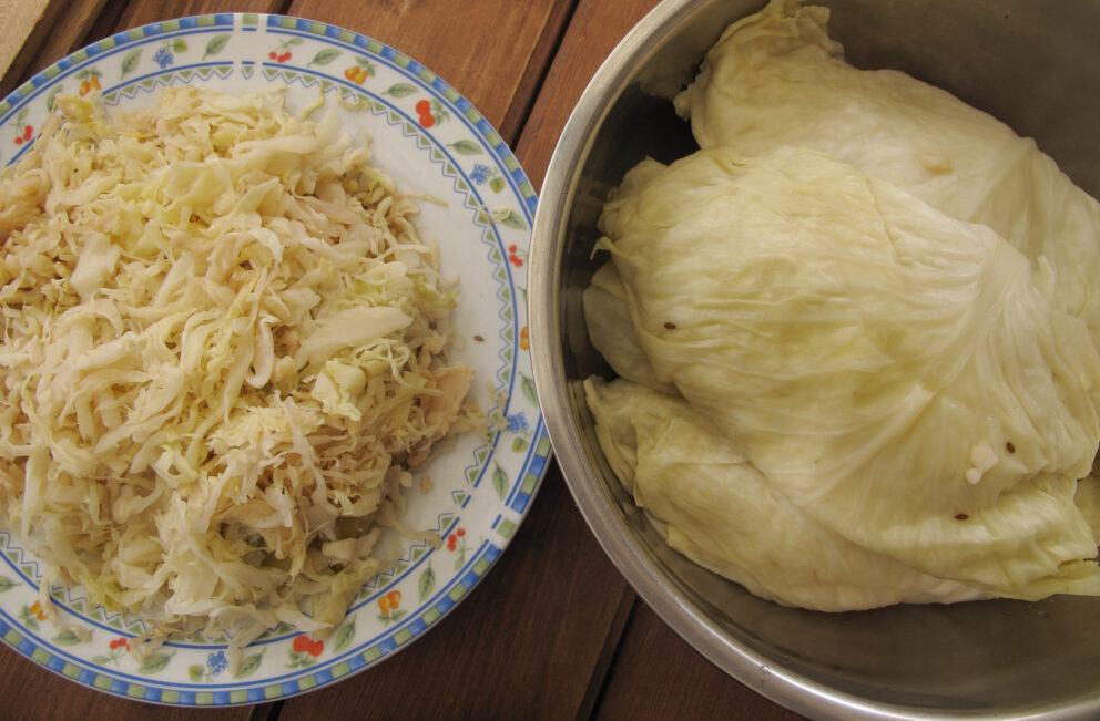A plate of shredded sauerkraut next to a bowl of whole cabbage leaves