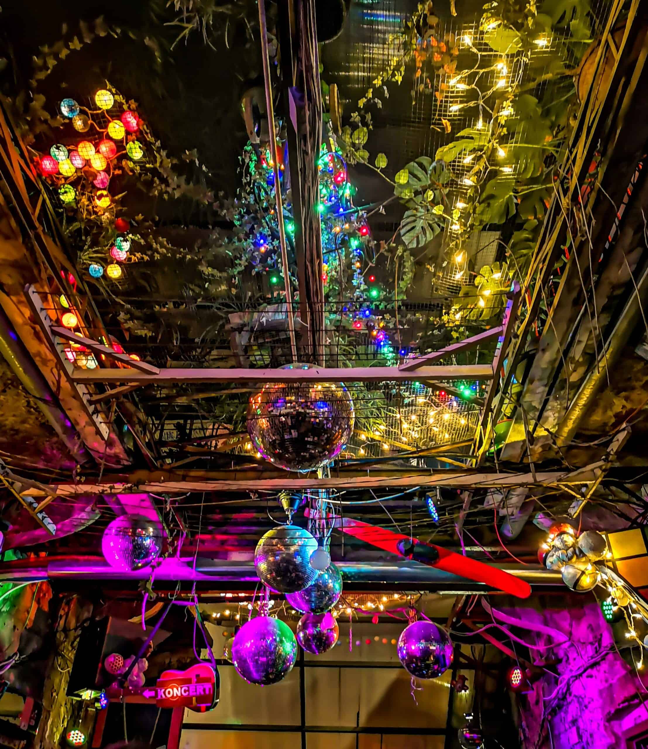 The surreal and colorful interior of Szimpla Kert ruin bar in Budapest, decorated with numerous disco balls and neon lights.