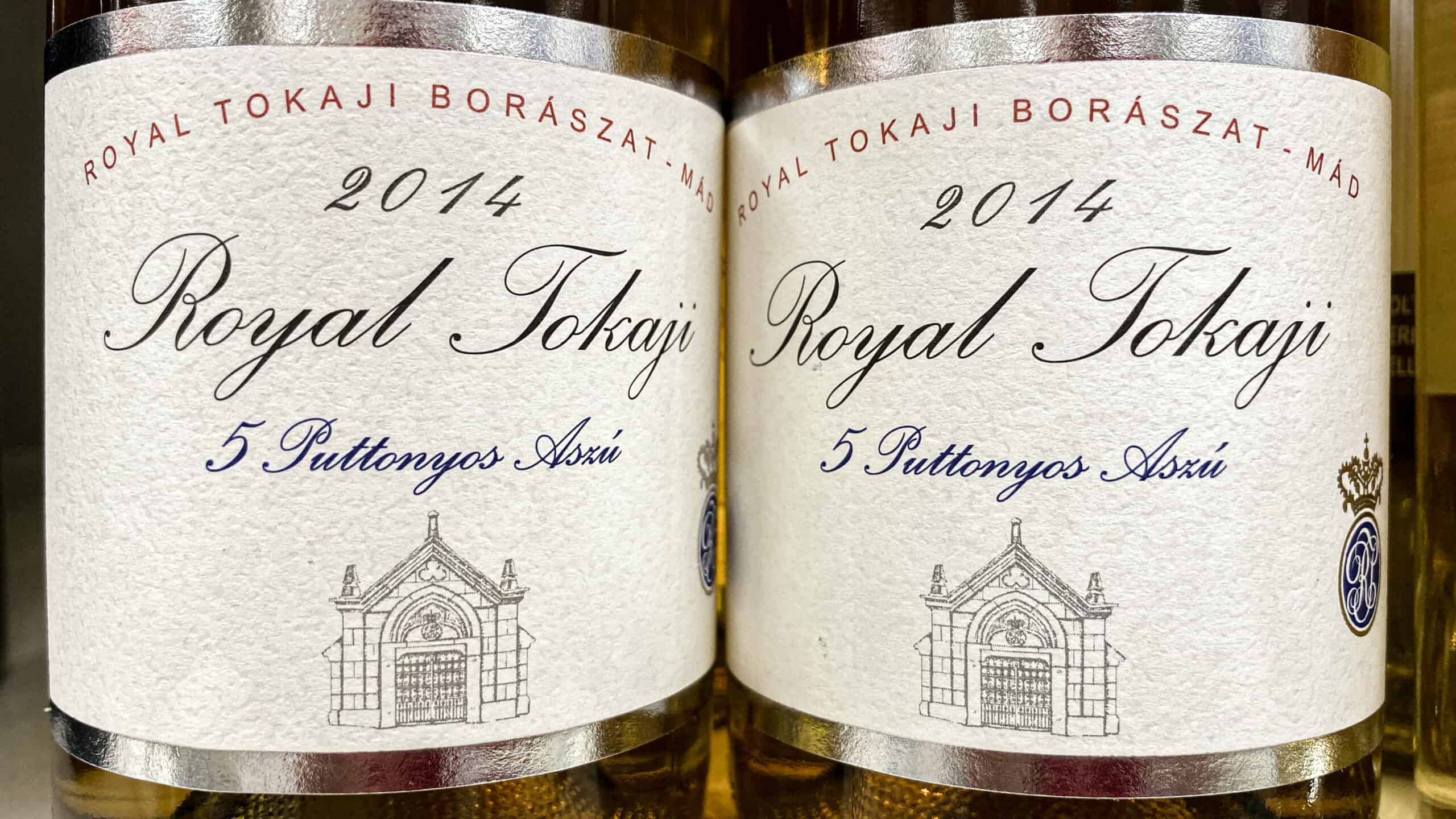 A bright golden glass and heavily labeled bottle of Tokaji Aszú sweet dessert wine