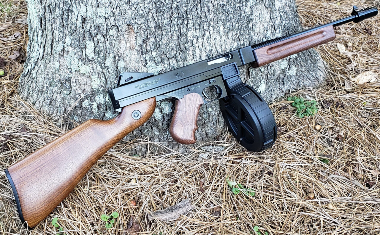A classic Tommy Gun with a round drum magazine leaning against a tree