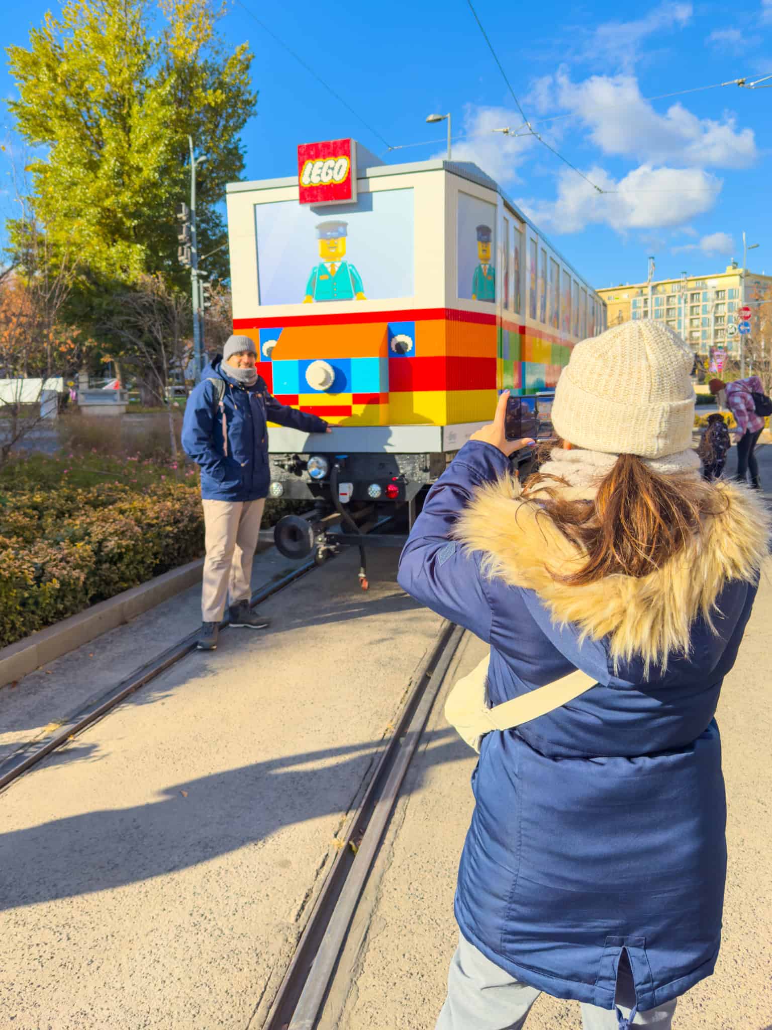 Excited tourists taking selfies directly with the massive yellow LEGO tram installation