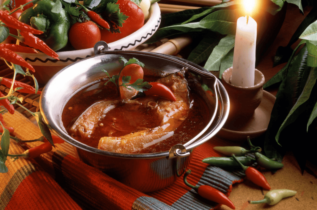 A rustic bowl of bright red traditional Hungarian Fisherman's Soup containing large pieces of carp