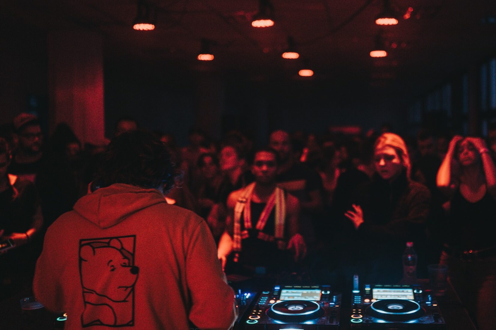 A DJ playing a dark underground techno party bathed in red light