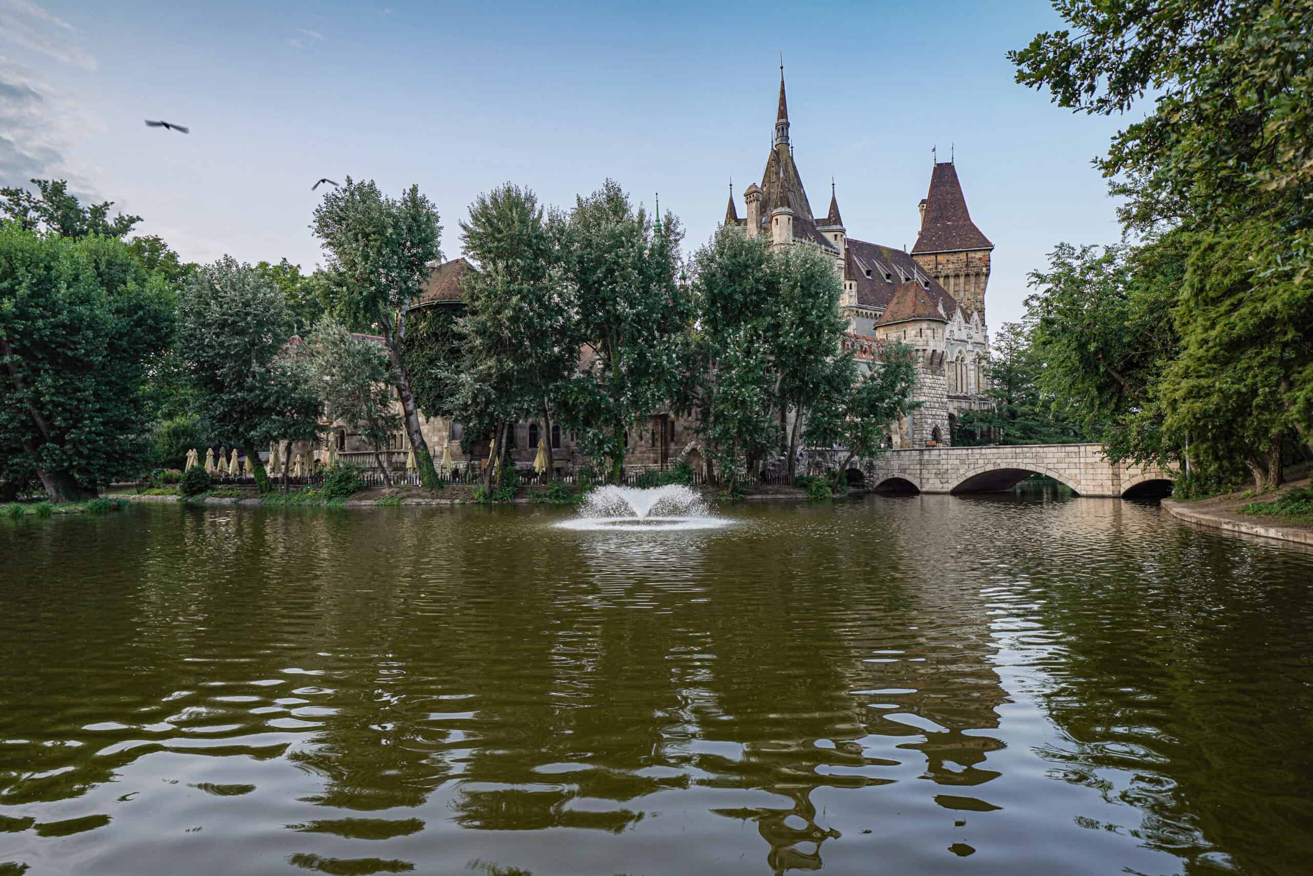The fairytale-like Vajdahunyad Castle reflected in the waters of the City Park lake with a fountain spraying.
