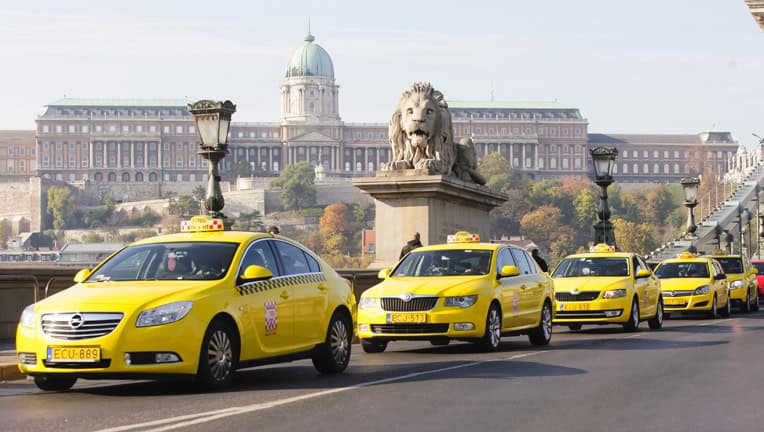 A bright yellow official taxi driving through the downtown streets of Budapest