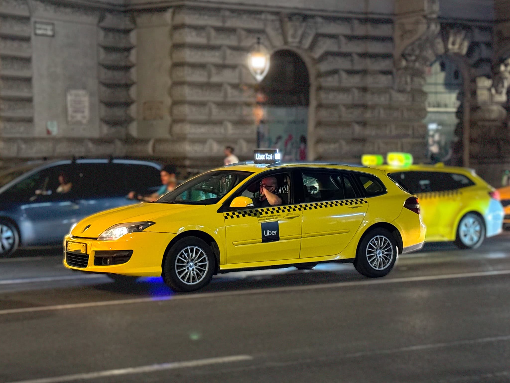 A yellow Uber taxi driving down a street at night