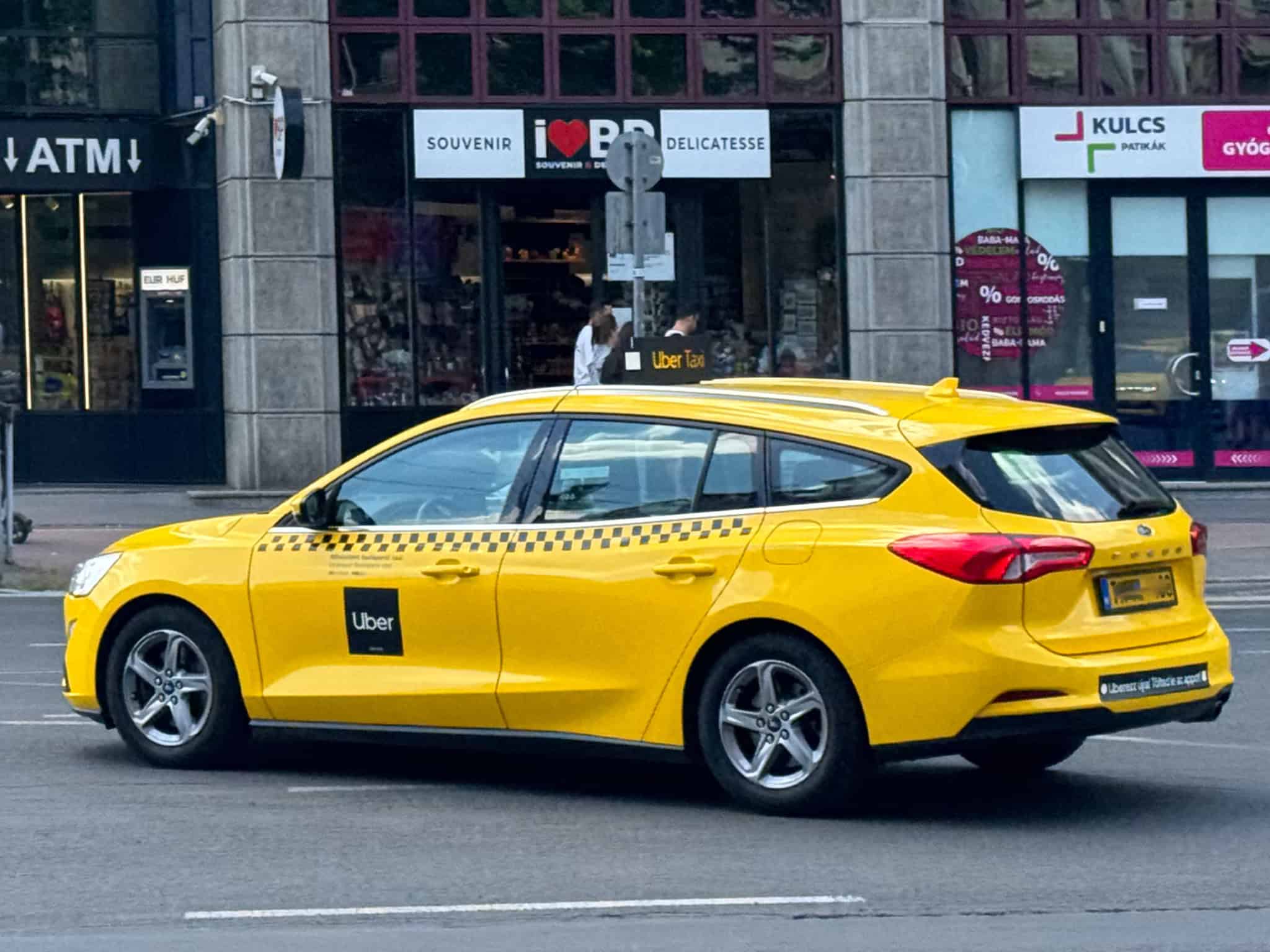 A yellow Uber taxi driving down a city street in Budapest